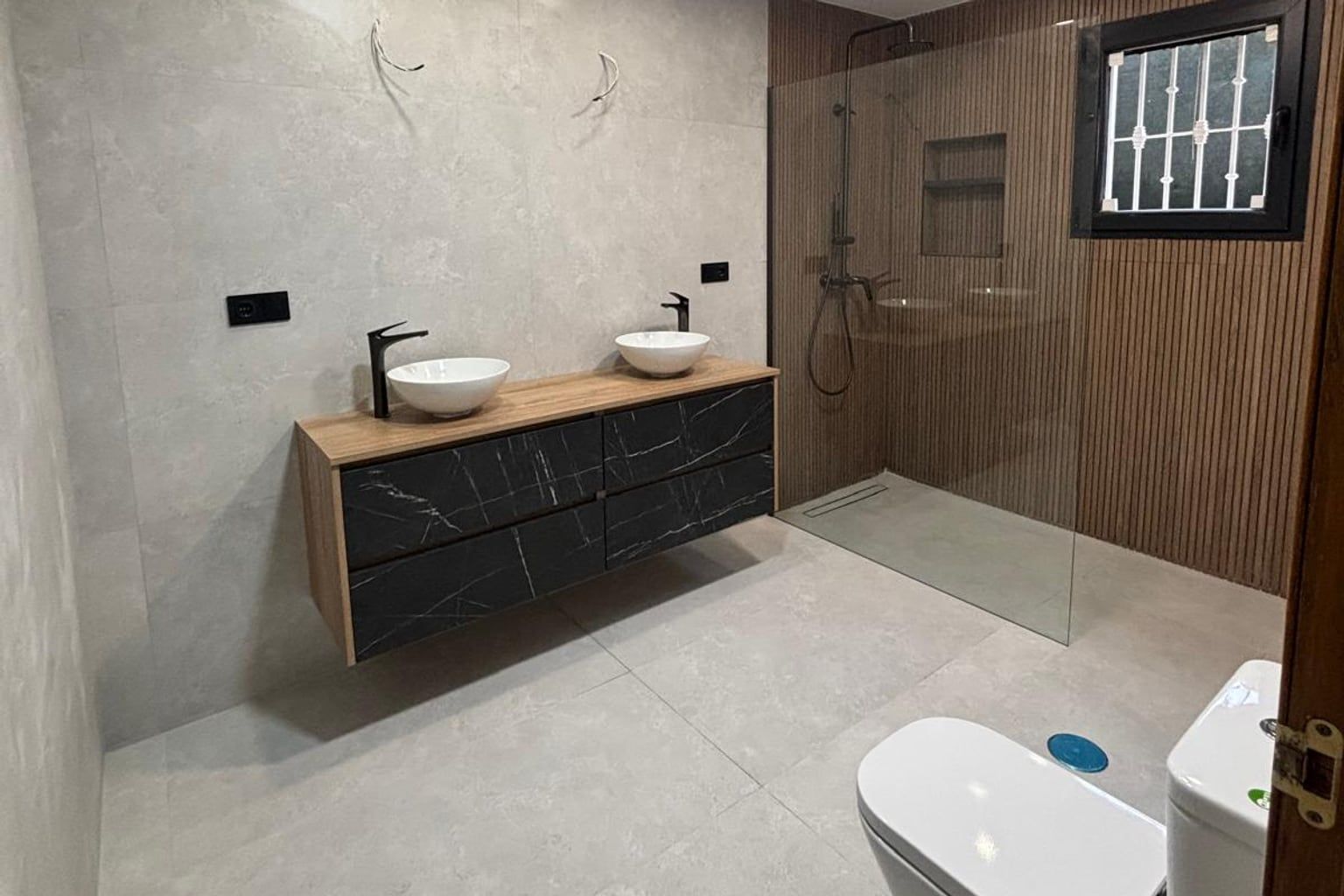 Baño reformado con doble lavabo, ducha de obra y pared de listones de madera
